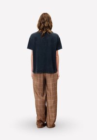 Zwarte katoenen t-shirt en losse, geruite broek in bruin, rood en crème, met een rechte snit en zichtbare plooien aan de achterkant.