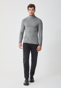 Suéter de cuello alto gris en una tela suave, combinado con jeans oscuros y botas negras de cordones. Diseño simple y ajustado con mangas largas.