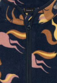 Marinblå fleecejacka med dragkedja, abstrakta mönster i gult, rosa och brunt, med hög krage och mjuk textur.