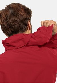 Giacca rossa con colletto alto e tessuto liscio e resistente all'acqua. Il colletto presenta un design flessibile, mentre il retro mostra dettagli di cucitura.