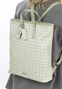 Sac à dos texturé vert clair avec motif géométrique, deux poignées supérieures, bretelles ajustables et un détail de porte-clés de marque.
