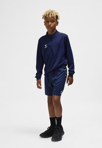 Nachtblauw sportief trainingspak met een zip-up top met lange mouwen en bijpassende korte broek, voorzien van grijze accenten en zwarte sneakers met hoge sokken.