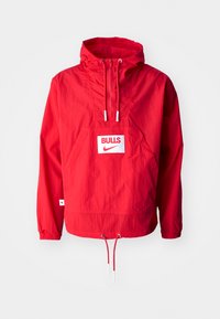 Röd Nike vindjacka med huva, framficka och justerbar dragsko i nederkant. Har en "BULLS"-logotyp på en vit lap. Slät textur.