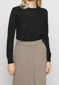 Czarny sweter z długim rękawem wykonany z miękkiego materiału, w połączeniu z brąską spódnicą w wzór houndstooth, z wysokim stanem i eleganckim krojem.