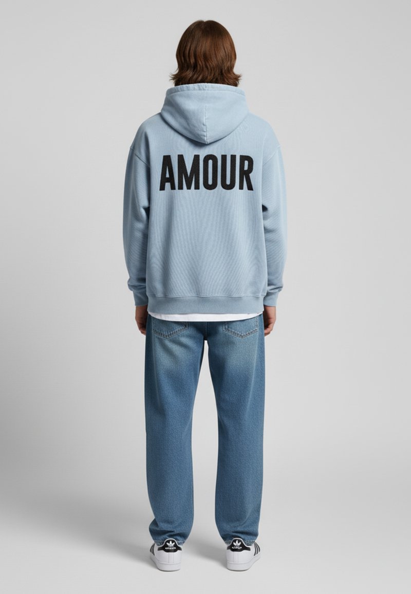 Felpa azzurra chiara con la scritta nera "AMOUR" sulla schiena, abbinata a jeans baggy azzurri chiari a vita alta e scarpe da ginnastica nere.