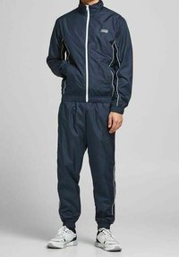 Chándal marinero con detalles en blanco, que incluye una chaqueta con cremallera y pantalones con cintura elástica. Fabricado en tejido liviano que absorbe la humedad.