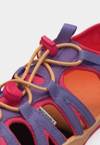 Μωβ και ροζ σανδάλι με μπεζ ελαστικά κορδόνια και κόκκινα κλείστρα, ανοιχτού σχεδιασμού, με ορατή ετικέτα από πλενόμενο ύφασμα στο εσωτερικό.