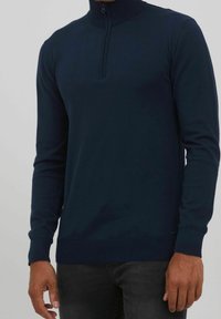 Granatowy sweter na zamek z gładkiego dzianiny. Posiada długie rękawy oraz ściągacz przy kołnierzu i mankietach, co zapewnia dopasowany krój.