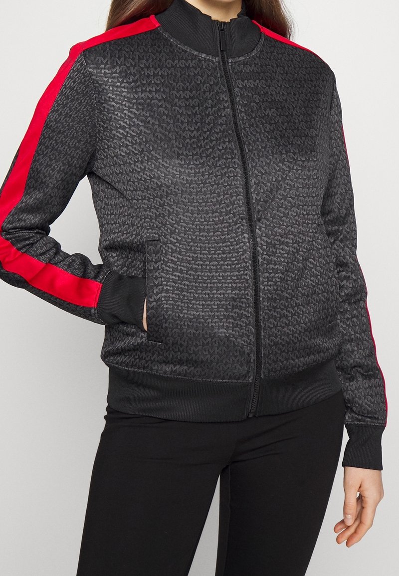 Svart zip-up jacka med ett texturerat mönster och röda sidostreck. Har en upprätt krage samt ribbade muddar och nederkant. Inkluderar sidofickor.