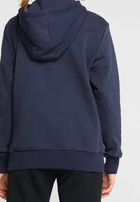 Sudadera azul marino hecha de un tejido suave, con un bolsillo frontal, puños y dobladillo acanalados texturizados, que presenta una capucha trasera grande y un corte relajado.