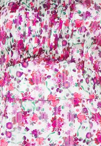 Tissu blanc avec un motif dense de petites fleurs roses, rouges et violettes ainsi que des feuilles vertes, avec des plis verticaux et une large ceinture.
