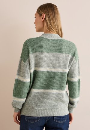 Sweter robiony na drutach w zielono-szare paski, z okrągłym dekoltem i ściągaczami przy mankietach. Miękka faktura i luźny krój, noszony z niebieskimi dżinsami.