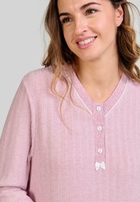Blusa de manga larga color rosa claro con canalé vertical, cuello redondeado, ribete blanco, tres botones y un pequeño lazo decorativo en el escote.