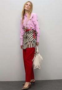 Camisa de manga larga rosa con estampado de perro, falda envolvente a rayas y con estampado, pantalones rojos, tacones con estampado de leopardo, bolso blanco.