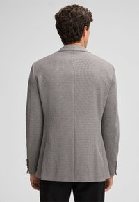 Szary blazer o teksturowanej fakturze w slim fit, z klapami, dwiema wentylacjami z tyłu i zapinanymi mankietami, pokazany od tyłu na jednolitym tle.