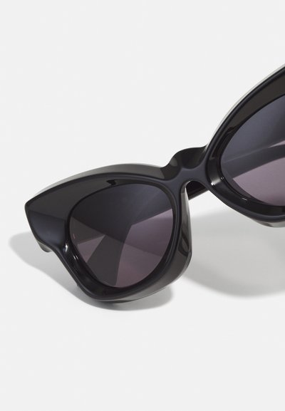 Occhiali da sole a occhio di gatto in plastica nera con lenti scure, caratterizzati da un design audace e angolare e punte pronunciate sui bordi esterni.