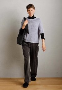 Person walking indoors wearing a gray sweater over black top, dark wide-leg pants, black shoes, and carrying a large black shoulder bag.