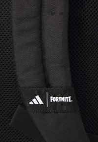 Juodas kuprinės maišas su tinklelio tekstūra ir paminkštintais dirželiais. Yra baltas "Fortnite" logotipas ir trys baltos juostelės ant reguliuojamo diržo.