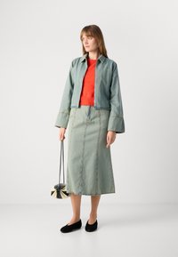 Lys blå denimjakke, oransje strikkegenser, lang lys blå denimskjørt og svarte leiligheter. Holder en liten svart og hvit veske.