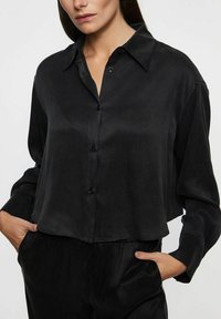 Sort satin skjorte med knapper, krave, lange ærmer og en afslappet pasform. Glat tekstur, let cropped kant og sorte knapper.