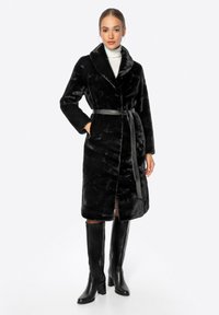 Černý kabát z umělé kožešiny se šálovým límcem, páskem v oblasti pasu, dlouhými rukávy a bočními kapsami. Doplňují ho černé vysoké boty po kolena.