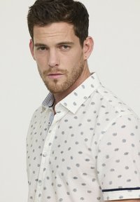 Witte korte mouwen blouse met een marineblauw stippenpatroon, voorzien van een gestreepte kraag en marineblauwe accenten op de mouwen, gemaakt van textuurstof.