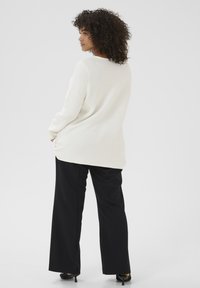 Knit cream sweater with ribbed texture, long sleeves, and relaxed fit paired with black wide-leg trousers and heels. Back view shown.