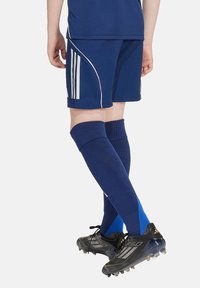 Marineblauwe sportshorts met witte strepen, gecombineerd met kniehoge marineblauwe-sokken met blauwe accenten, en zwarte voetbalschoenen met zilveren details.