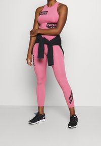Top corto deportivo rosa y leggings con acentos del logo negro "Nike". Diseño ajustado, textura suave, combinados con zapatillas deportivas negras.