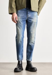 Blå denimjeans med en smal passform, med slitte lapper og bleking. Kombinert med svarte ankelstøvler.