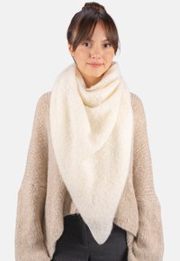 Écharpe triangulaire couleur crème en tissu doux et texturé. Portée drapée autour du cou, complétant un pull beige.