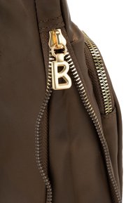 Brun tygväska med guldfärgade detaljer, med en framträdande "B" dragkedja, texturerad yta och kontrasterande dragkedjesmycken.