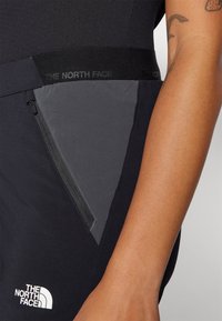 Črne kratke hlače z žepom na zadrgo in pasom, na katerem je v črni barvi izvezen napis "THE NORTH FACE". Material je gladek, s kontrastno sivo ploščo.
