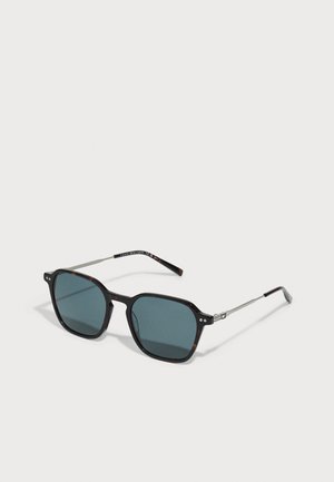 Occhiali da sole con montatura ottagonale scura, lenti blu, stanghette metalliche sottili e dettagli in tartaruga sui lati esterni.