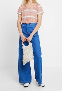 Top de algodón con estampado y mangas cortas, combinado con unos jeans amplios de color azul. Accesorio: bolso de punto blanco con un asa redonda.