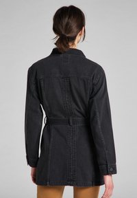 Svart denimjacka med bälte i midjan, en något överdimensionerad passform och knäppta manschetter. Har sömnad och en klassisk krage.