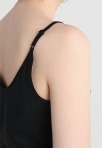 Zwarte tanktop met dunne schouderbandjes, zachte katoenmaterialen, een aansluitend ontwerp en een eenvoudige, effen textuur. Geen zichtbare patronen of accenten.