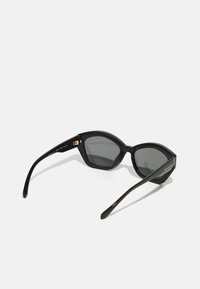 Melni saulesbrilles ar ģeometrisku rāmi, pelēkiem objektīviem un zelta akcentiem uz eņģēm. Rokas ir elegantas un nedaudz izliekta formas.