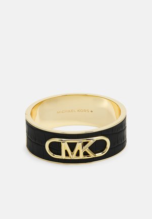 Bransoletka typu bangle w złotym odcieniu z czarną fakturowaną wstawką i wypukłym logo "MK" z przodu, wewnątrz wygrawerowano nazwę "Michael Kors".