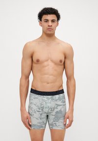 Boxeri pentru bărbați, cu un model de camuflaj gri deschis, confecționați dintr-un material elastic, cu un elastic lat de culoare neagră, care are inscripționat în relief textul "ARMOUR".