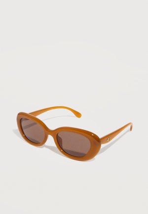 Gafas de sol ovaladas marrones con montura gruesa y lentes tintadas oscuras, descansando sobre una superficie blanca.