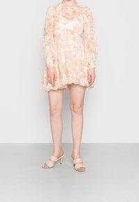 Blommig mini-klänning i blek orange och vitt, långa ärmar, volangkjol, lagerdesign. Tillsammans med bleka beige klackmule.