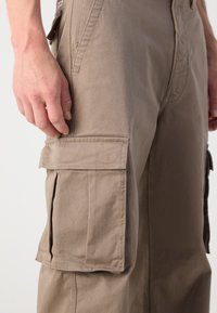 Brune cargo bukser med sidelommer, fremstillet af et holdbart bomuldsblandingsstof, med syninger i detaljerne og en afslappet pasform. Glat tekstur tydelig.