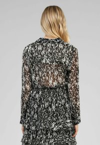 Robe à motifs noir et blanc avec un tissu transparent, un ourlet volanté et un col. Dispose d'une taille à cordon de serrage et de manches longues.