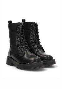 Botas de combate de cuero negro con caña acolchada, cordones en la parte delantera y suela de goma texturizada. Presentan tiradores para facilitar su uso y costuras reforzadas.