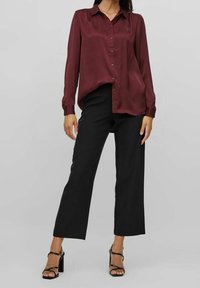 Burgundy satin button-up shirt with long sleeves, paired with black wide-leg trousers and black block-heeled sandals.