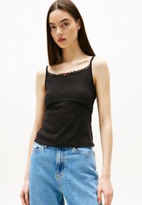 Top negro de canalé con bordado de encaje en el escote y un pequeño acento rojo, combinado con jeans de mezclilla azul claro.