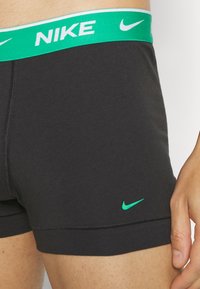 Shorts da boxer neri con una fascia verde e il logo "NIKE" in bianco. Ulteriore logo a forma di swoosh verde sul lato sinistro in basso. Texture liscia.