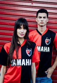 Zwart en rode voetbalshirts met korte mouwen, voorzien van een logo aan de linkerkant en het woord "YAMAHA" in vetgedrukte witte letters.