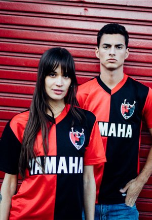 Zwart en rode voetbalshirts met korte mouwen, voorzien van een logo aan de linkerkant en het woord "YAMAHA" in vetgedrukte witte letters.